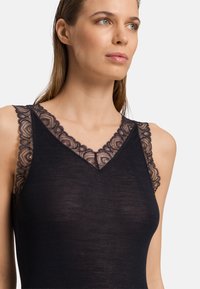 Svart ribbad tanktop med delikat blommönstrad spets längs halsringningen och axelremmarna, med en figurnära passform och mjuk textur.