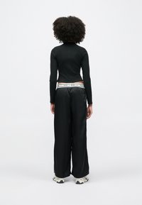 Μαύρο μακρυμάνικο τοπ με ριμπ ύφανση, συνδυασμένο με φαρδιά μαύρη παντελόνια που έχει λευκή ζώνη της Nike και πλευρικά φερμουάρ. Παπούτσια αθλητικά σε ανοιχτό χρώμα.