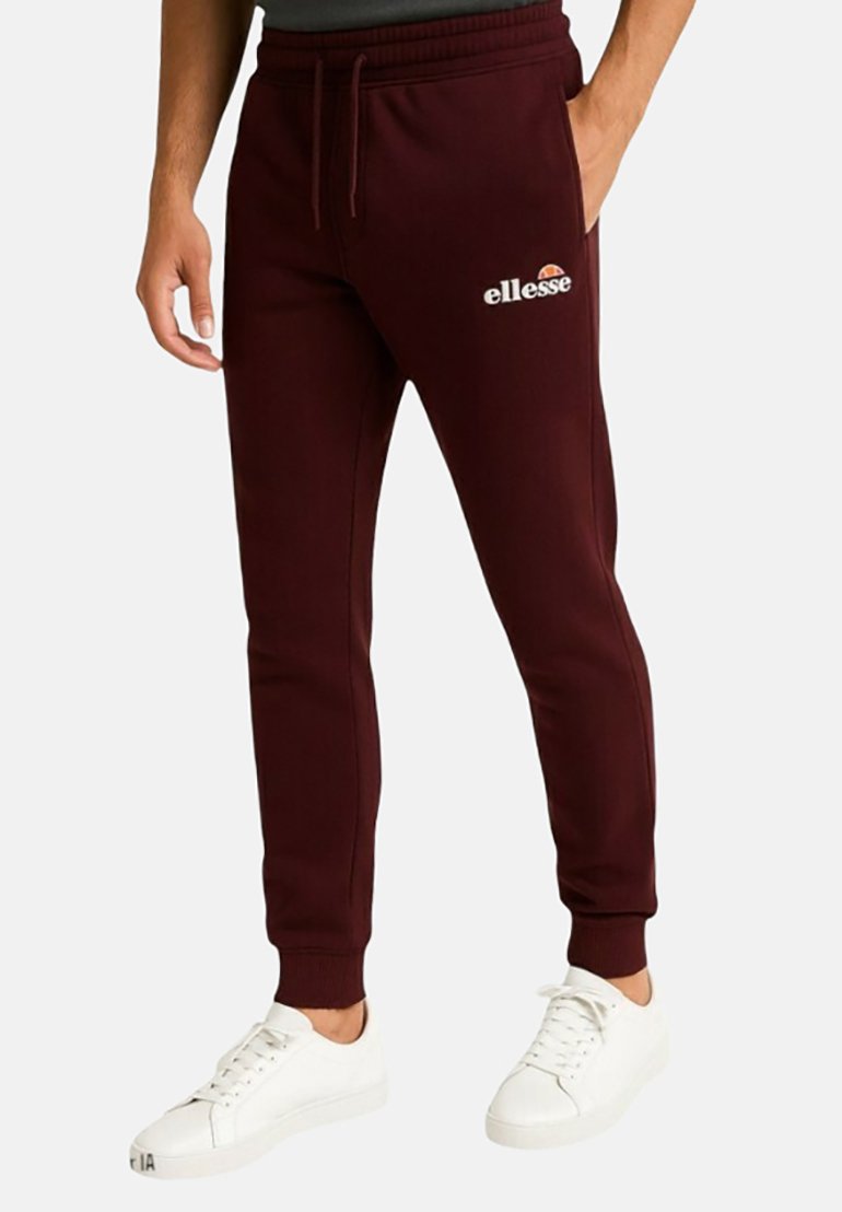 Joggeurs bordeaux avec taille élastique, ourlets resserrés, poches latérales, et logo blanc "ellesse" sur la cuisse gauche. Portés avec des baskets blanches.