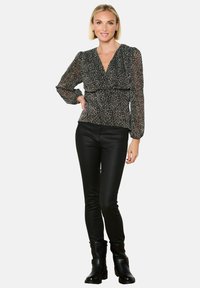 Blusa nera con stampa leopardata, maniche lunghe, scollatura a V e vita arricciata, abbinata a pantaloni neri con taglio slim e stivali alla caviglia.