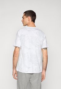 White short-sleeve t-shirt with a light gray abstract pattern, crew neck, smooth fabric, and a relaxed fit, shown from the back.