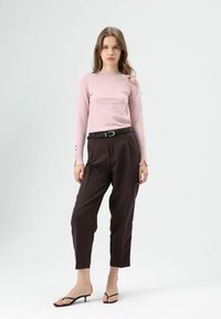 Lichtroze top met lange mouwen en knoopdetails, gecombineerd met hooggetailleerde bruine broek en zwarte sandalen met bandjes. Eenvoudig, modern ontwerp.