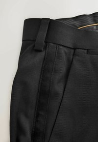 Schwarze Anzughose aus strukturiertem Gewebe, mit flacher Vorderseite, Gürtelschlaufen und glattem Bund. Details umfassen seitliche Nähte.