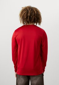 Rotes Langarmshirt aus glattem Stoff. Rundhalsausschnitt-Design mit lockerer Passform und Nähten entlang der Schultern und Ärmel.