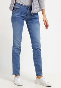 Ljust blå denimjeans med slim fit, som har fem fickor och subtil blekning. Kombinerat med vita sneakers och en grå topp.