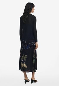 Black knit long-sleeve sweater paired with a flowy, patterned black skirt featuring colorful floral designs. Minimalist black heel sandals.