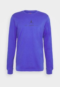 Lila långärmad tröja med svart Jordan-logotyp och liten tryckt text centrerad på bröstet, rundad halsringning och ribbade muddar.
