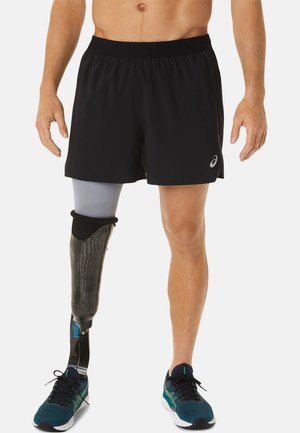 Black athletic shorts worn by a person, featuring a prosthetic leg with a carbon fiber design and blue accent, paired with teal running shoes.