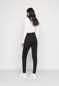 Calças jogger pretas com cintura elástica, bolsos laterais e pernas ajustadas, combinadas com uma blusa justa de manga longa branca.