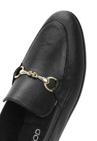 Mocassino in pelle nera con punta rotonda, caratterizzato da un dettaglio in metallo dorato e una finitura texturizzata. Fodera morbida e suola piatta per il massimo comfort.