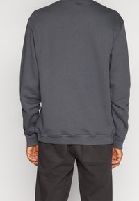 Šedá mikina s dlouhými rukávy, kulatým výstřihem, žebrovanými manžetami a spodním lemem. Hladká textura látky, jednoduchý design, žádné viditelné vzory ani akcenty.