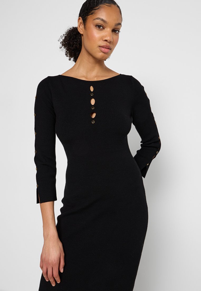 Zwarte ribgebreide jurk met een ronde hals, driekwartmouwen en decoratieve gouden knopen langs de sluiting en manchetten.