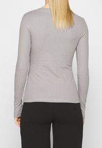 Top a maniche lunghe in maglia a coste di colore grigio chiaro, con una silhouette aderente e una consistenza morbida, abbinato a pantaloni neri.