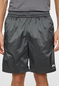 Svarta sportshorts för män, tillverkade av lättviktsmaterial med en glänsande yta. De har resårmidja och sidofickor samt en liten logotyp på fållen.