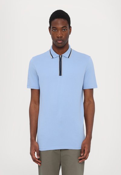 Lyseblå polo shirt med en lynlås krave, der har en sort og hvid accentstribe. Korte ærmer og en glat tekstur. Casual pasform.
