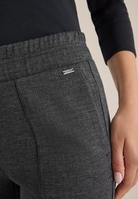 Grijze broek met een visgraatpatroon, voorzien van een zachte textuur, elastische tailleband en een klein zilveren logo-label op de voorkant van de zak.