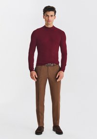 Bordowa dopasowana koszula z długim rękawem w połączeniu z brązowymi spodniami. Strój charakteryzuje się gładkimi fakturami i okrągłym dekoltem. Całość dopełniają brązowe buty.