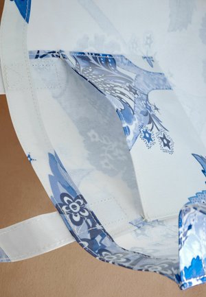 Sac en textile bleu et blanc orné de motifs floraux, doté d'une poignée en tissu et d'une texture subtile avec des coutures renforcées.