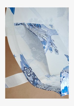 Sac en textile bleu et blanc orné de motifs floraux, doté d'une poignée en tissu et d'une texture subtile avec des coutures renforcées.