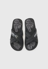 Black flip-flops with cross straps, textured surface, and logo detail. Soft material with padded footbed and standard flat sole design.