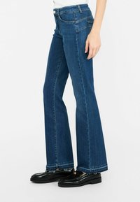 Jeans in denim blu a gamba svasata con vita alta, caratterizzati da cuciture classiche, design a cinque tasche e dettagli con orlo sfrangiato.