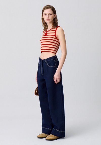 Crop top a righe rosse e beige con scollatura rotonda, abbinato a pantaloni a gamba larga blu navy con cuciture a contrasto, e scarpe beige slip-on.
