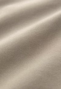 Bežna tkanina glatke teksture i suptilnim rebrastim uzorkom, prikazana u mekim, valovitim naborima, naglašavajući svoju fleksibilnu draperiju.