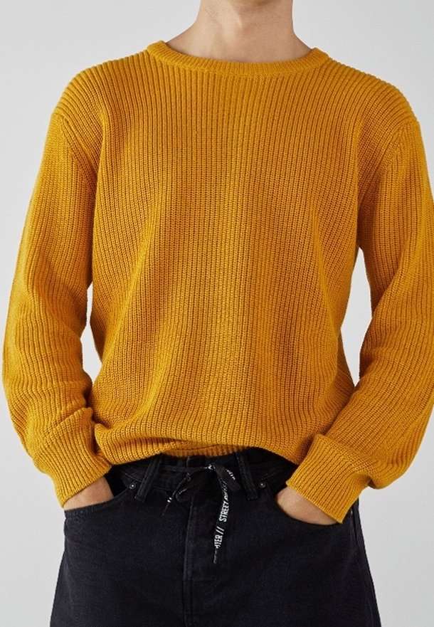 Gelber Strickpullover mit Rundhalsausschnitt, gerippter Textur und langen Ärmeln, kombiniert mit schwarzen Jeans mit einem Kordelzugbund.