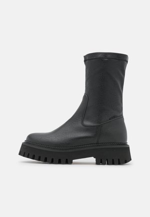 Botte noire en cuir mi-mollet avec semelle épaisse à crampons et bout arrondi, avec des coutures discrètes et une finition lisse et texturée.