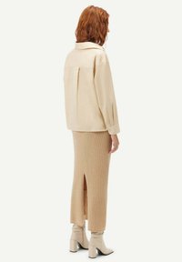 Beige oversized skjortjacka med en ryggveck, kombinerad med en ribbad beige midiklänning med en sidoklyfta, och ljusa klackstövlar.