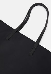 Black tote bag made of smooth fabric, featuring two flat, matching straps. The design is minimalist with no visible hardware or patterns.