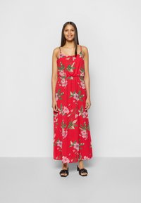 Vestido maxi floral vermelho com alças finas, apresentando uma cintura franzida. Possui um estampado de flores cor-de-rosa e folhas verdes, feito de um tecido leve.