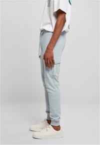 Lys blå joggebukser med elastisk midje, snøring, sidelommer og ribbestrikkede mansjetter; kombinert med hvite joggesko.