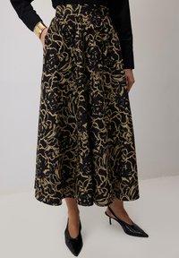 Črna krilna obleka z zlatim cvetličnim vzorcem, nabranim dizajnom in visokim pasom. Nosena z črnimi špicastimi petkami in črnim dolgim rokavom.