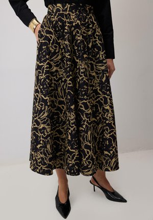 Fekete szoknya arany virágmintával, plisszírozott kialakítással és magas derékkal. Fekete hegyesorrú magassarkúval és fekete hosszúujjú toppal viselve.