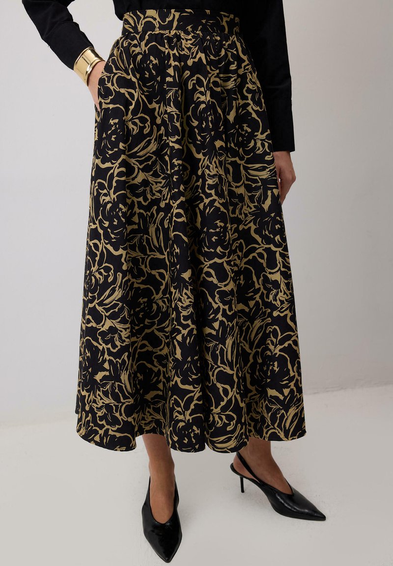 Črna krilna obleka z zlatim cvetličnim vzorcem, nabranim dizajnom in visokim pasom. Nosena z črnimi špicastimi petkami in črnim dolgim rokavom.