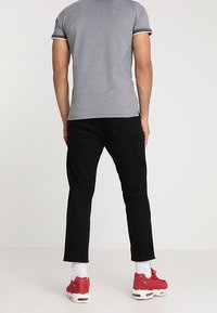 Šedá polo tričko s černými akcenty, černé džíny a červené tenisky. Tričko má fitted design a krátké rukávy.