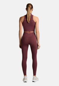 Fialovoružový atletický crop top v kombinácii so zodpovedajúcimi legínami s vysokým pásom. Disponuje kontrastnými oranžovými detailmi a štýlovým, priliehavým strihom.