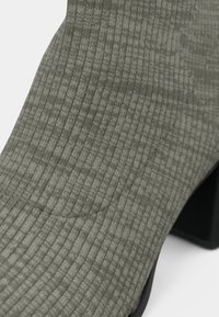 Primer plano de una bota de calcetín de punto acanalado en gris con tacón cuadrado, resaltando la textura y la forma del tejido.