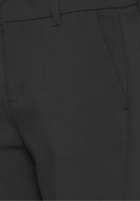 Gros plan d'un pantalon noir montrant la poche avant, la boucle de ceinture et les détails de couture sur un tissu lisse.