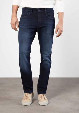 Dark blue denim jeans with a slim fit, featuring a classic five-pocket design and subtle stitching details. Paired with beige sneakers.