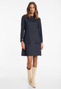 Gestreiftes Navy-Kleid aus Stoff, mit langen Ärmeln, hohem Kragen und zwei vorderen Taschen mit Knopfdetails.