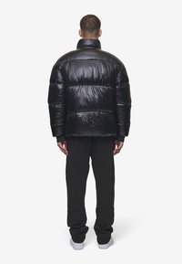 Sort puffer-jakke med høj krave, quiltet design og skinnende overflade. Båret over sorte sweatpants og hvide sneakers.