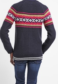 Jersey de color azul marino con un patrón geométrico colorido en rosa, amarillo y blanco en los hombros; puños y dobladillo acanalados.