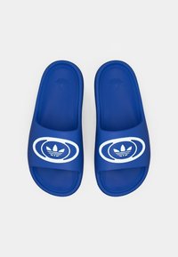 Modré gumové šľapky majú široký remienok s bielym grafickým logom a kruhovým dizajnom. Štruktúrovaná stielka poskytuje priľnavosť a pohodlie.