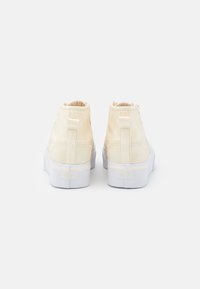 Höga sneakers i ett mjukt gult material med texturerade accenter, med en vit gummisula och minimal branding på baksidan.