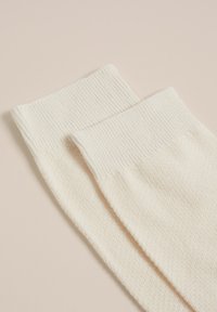 Ecrufarbene Socken mit strukturiertem Körper und gerippten Bündchen, aus einem weichen Material gefertigt. Zwei Paar werden gezeigt, flach auf einem neutralen Hintergrund liegend.