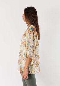 Blusa floreale leggera con una combinazione di colori pastello, vestibilità relax e maniche a batwing, realizzata in un tessuto morbido e semi-trasparente.