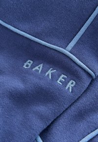 Sinine kangas pehme tekstuuriga, millel on helesinine aktsent ja tikandiga tekst "BAKER" kontrastse tooni sees.