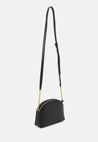 Svart läder crossbody-väska med en böjd form, guldkedjeprydnader och justerbar rem. Har en dubbel dragkedjestängning.
